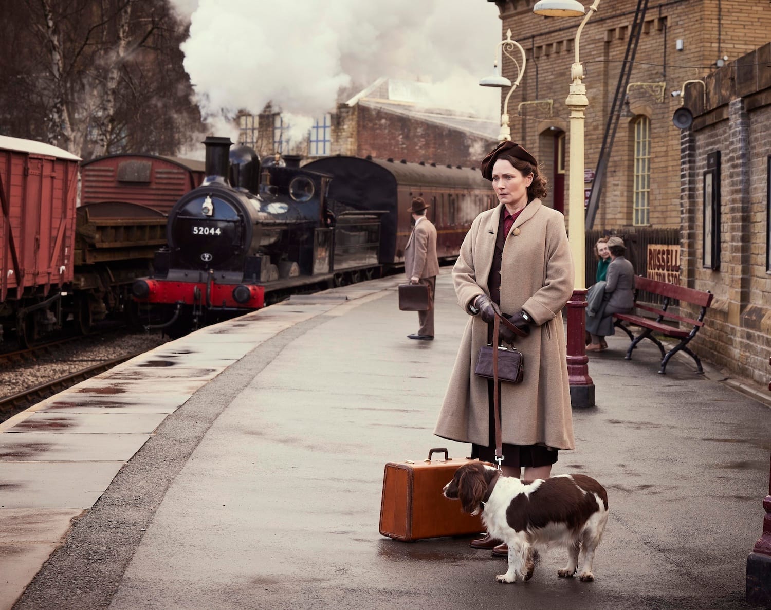 Audrey Hall stands the platform of  Darrowby station as a train steam pulls up. She's accompanied by her spaniel Dash and has a small suitcase.