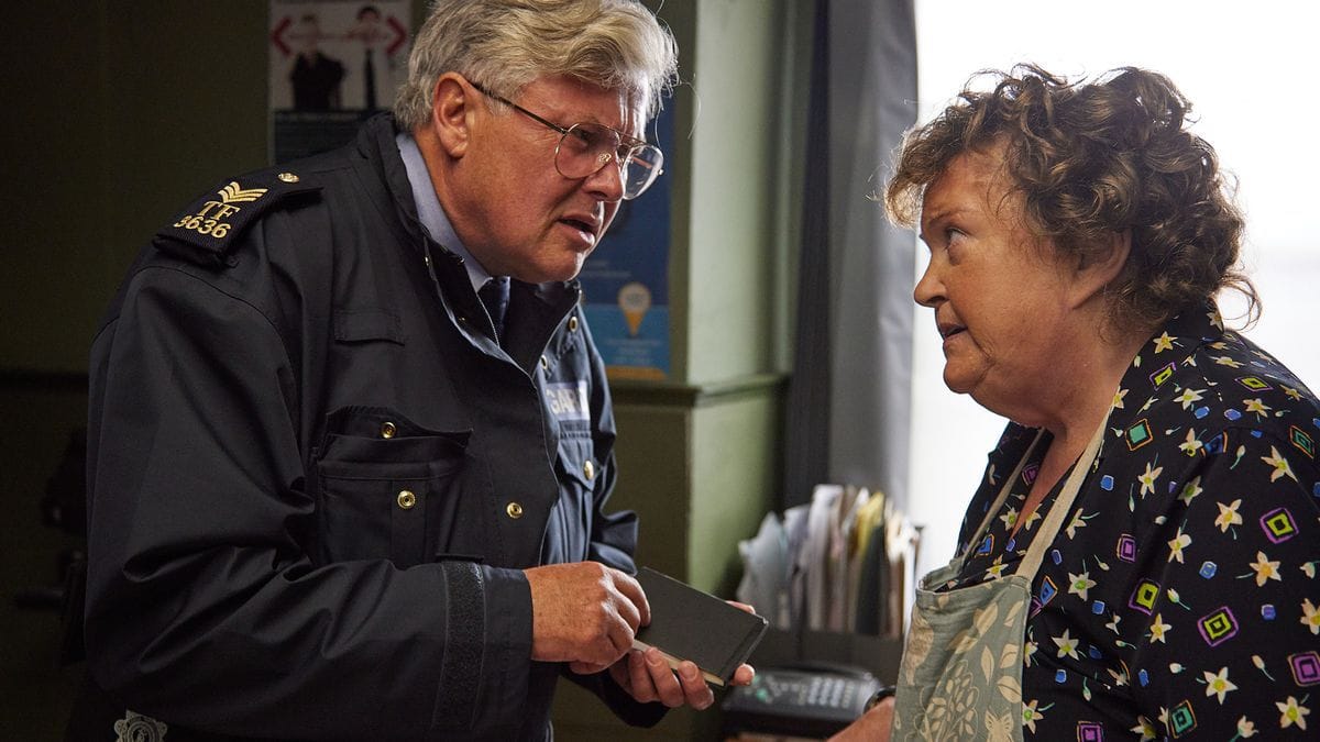 P.J. Collins (Conleth Hill) talking to Mrs. Meaney (Brenda Fricker), his surprise witness.