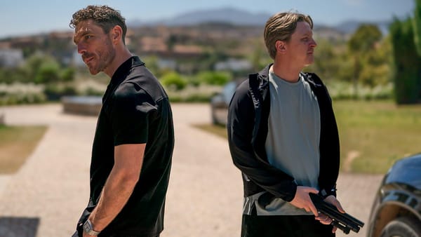 Michael (James Nelson-Joyce) and Banksey (Mike Noble), with a gun, guard the compound.