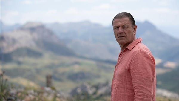 Ronnie Phelan (Sean Bean) stands in a rocky Spanish landscape.