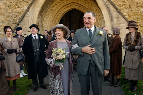 Both smiling, Mr. and Mrs. Carson (Jim Carter and Phyllis Logan) leave the church surrounded by well-wishers
