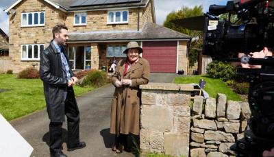 Blethyn and Leon stand casually together in front of a house, smiling at something off camera